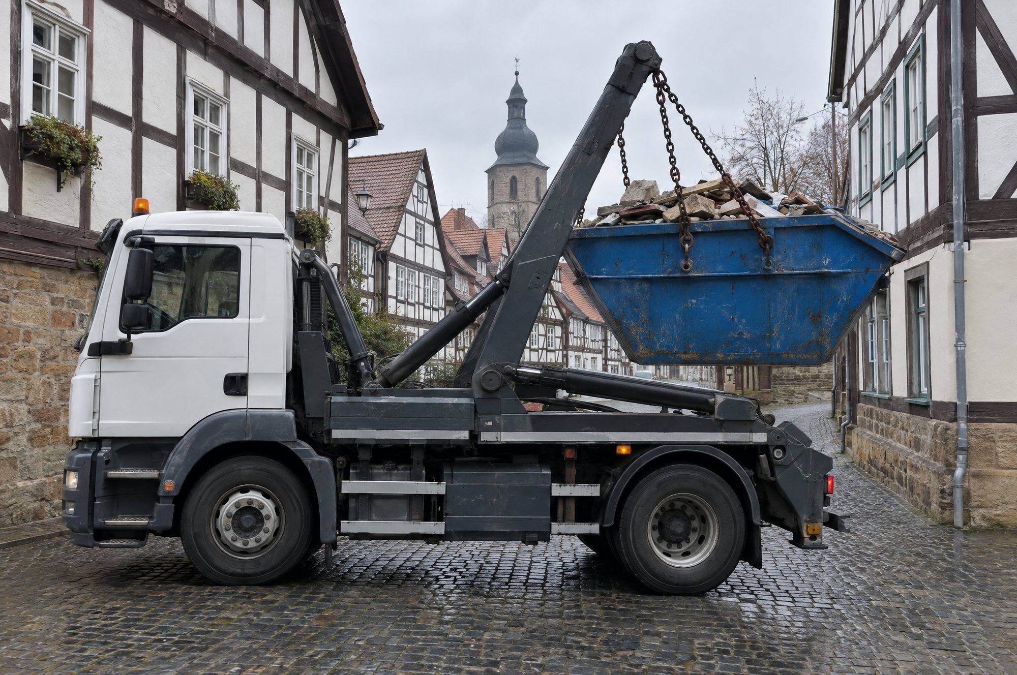 Absetzkipper hebt den vollen Container in einer engen Gasse mit Fachwerkhäusern an