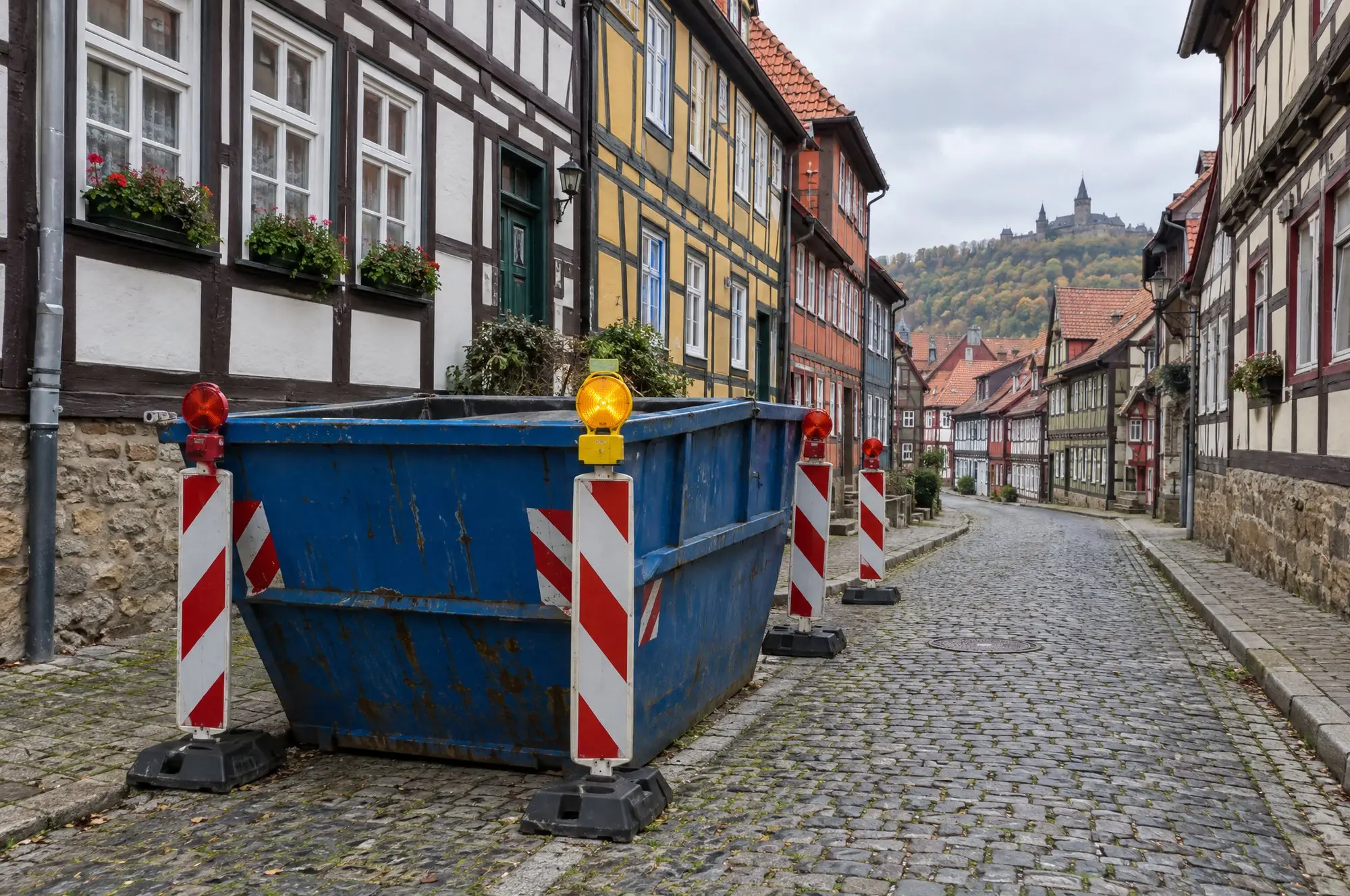 Container auf dem Parkstreifen einer Altstadtgasse, gesichert mit Leitbaken und Warnleuchte