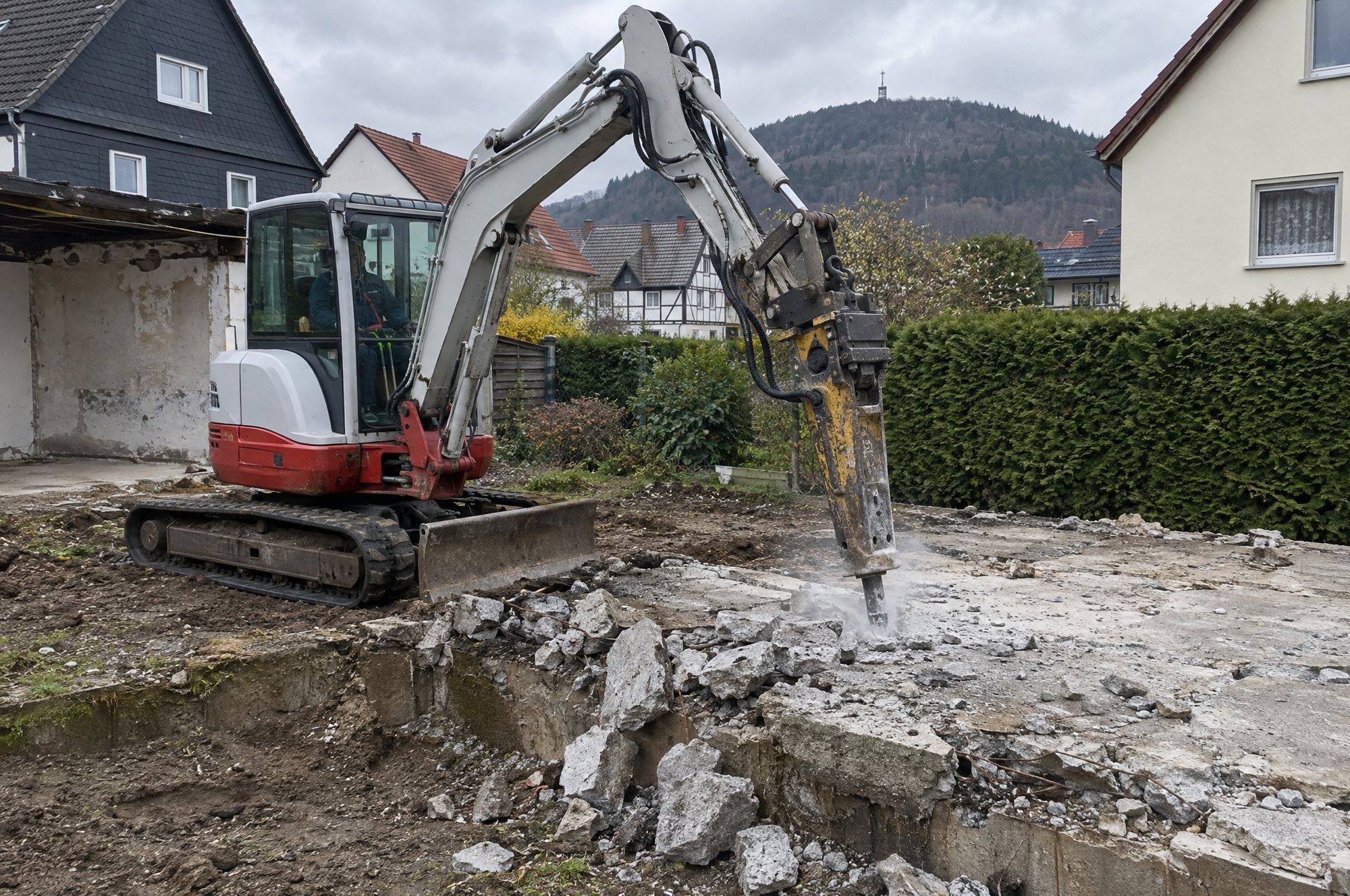 Minibagger mit Hydraulikhammer bricht die Betonplatte einer abgerissenen Garage auf