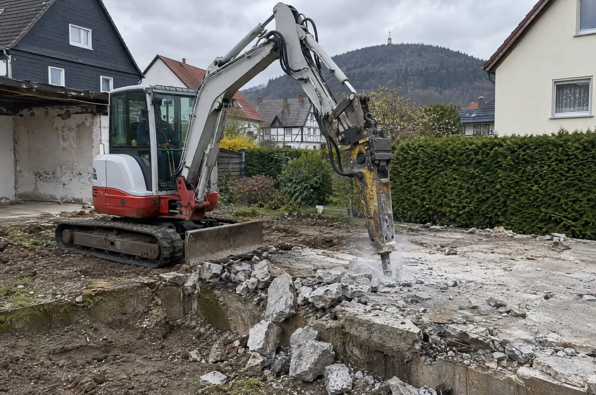 Minibagger mit Hydraulikhammer bricht die Betonplatte einer abgerissenen Garage auf