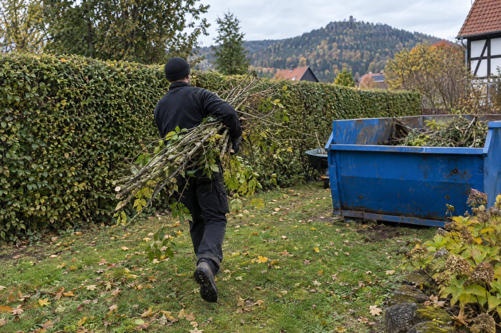 Mitarbeiter trägt ein Bündel Äste durch den Garten zum Container