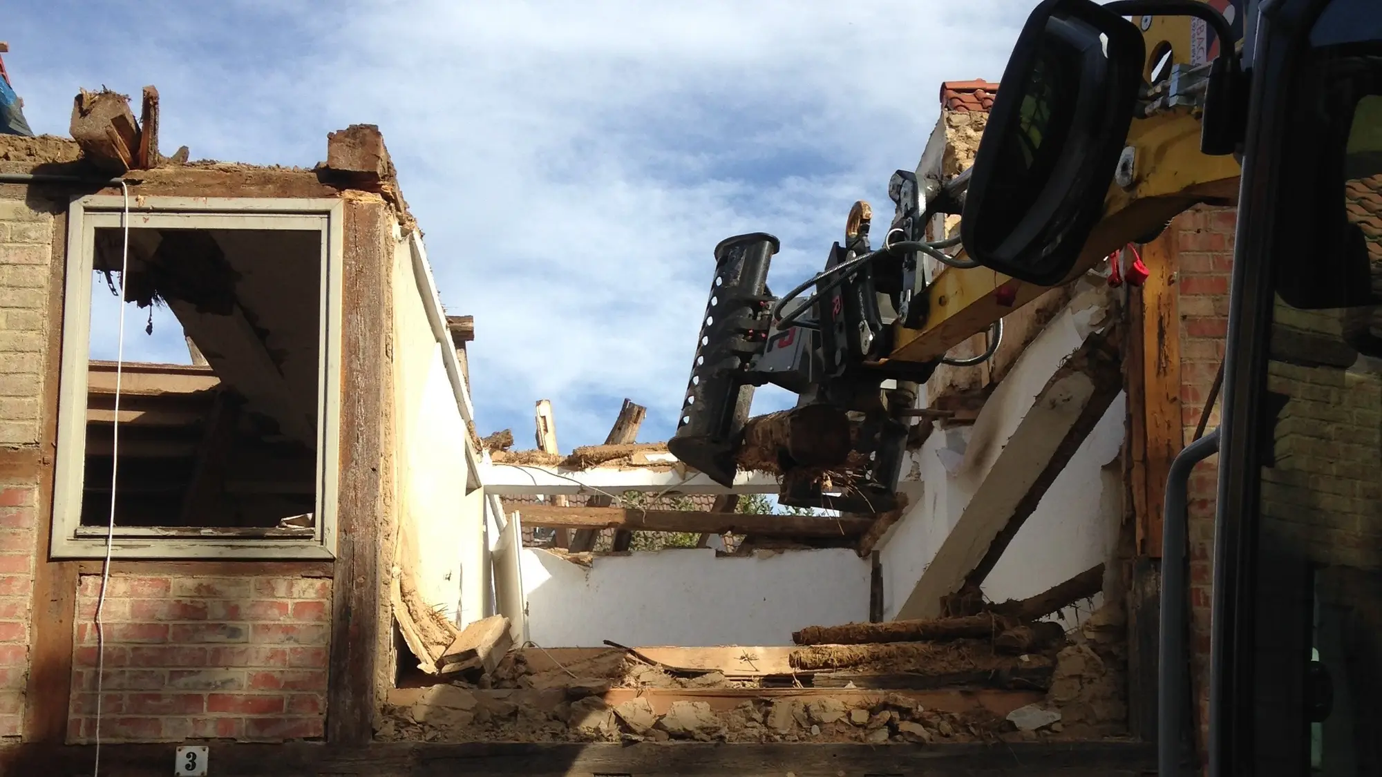 Bagger trägt die Giebelwand eines alten Wohnhauses ab, Fensteröffnung und Fachwerk sind noch zu sehen