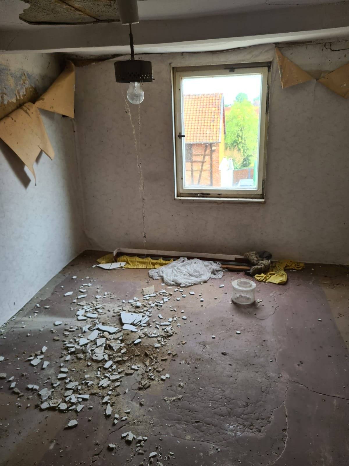 Entkernter Raum im Obergeschoss: Tapeten abgelöst, Putzreste auf dem Boden