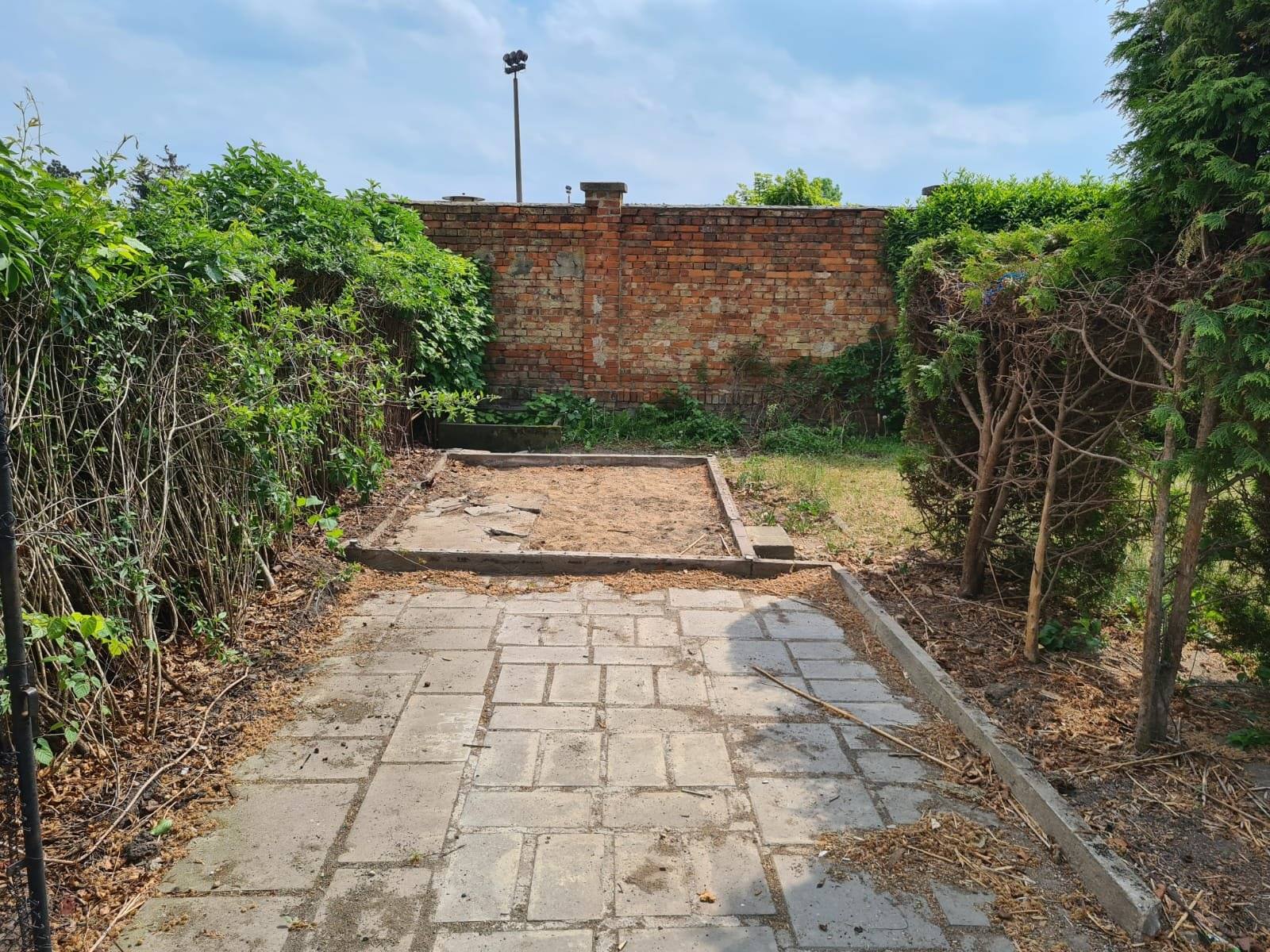 Beräumter Gartenweg aus Betonplatten zwischen Hecken bis zur Grundstücksmauer