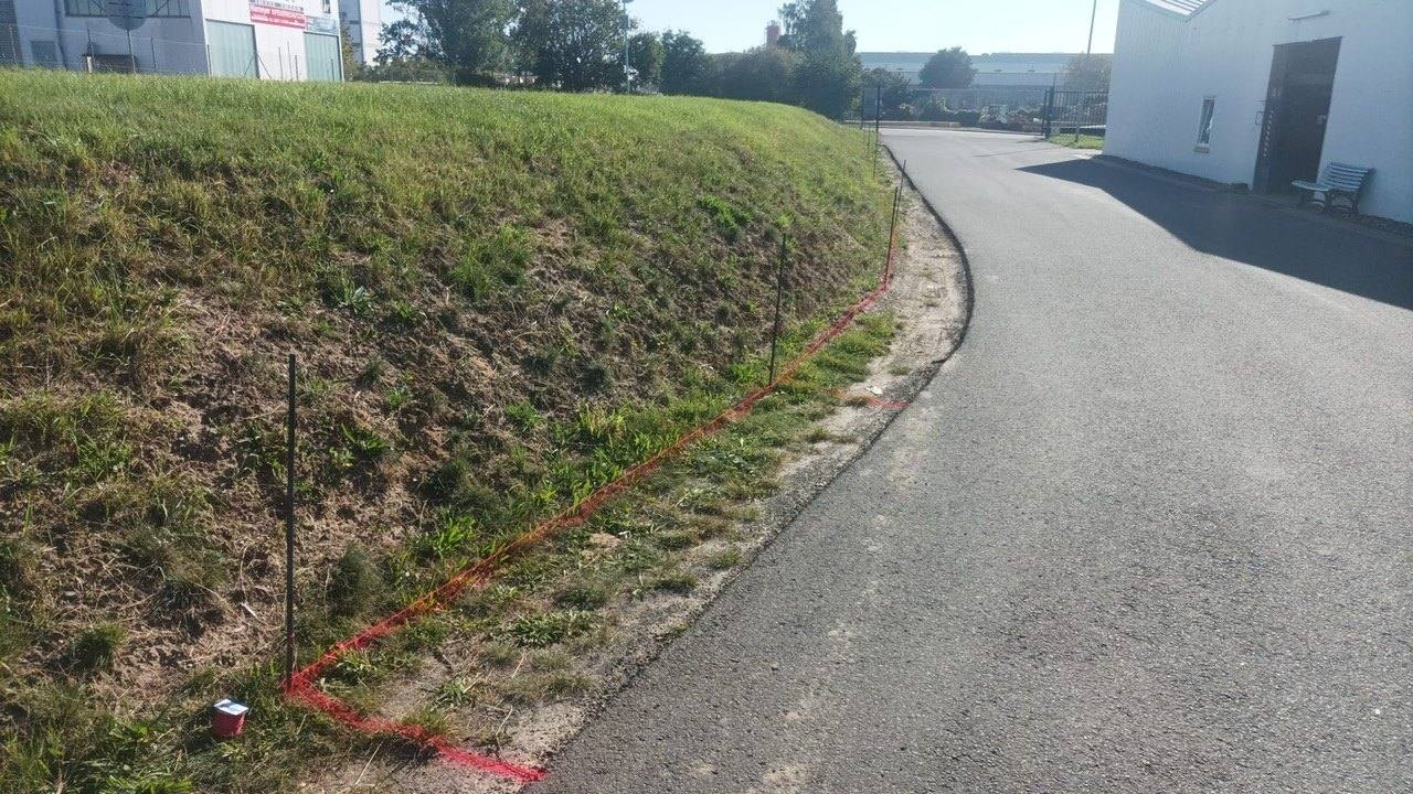 Rasenböschung entlang einer asphaltierten Gewerbestraße, die Arbeitsfläche ist rot markiert