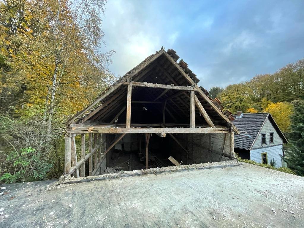Giebel einer Fachwerkscheune mit offenem Dach vor Herbstbäumen