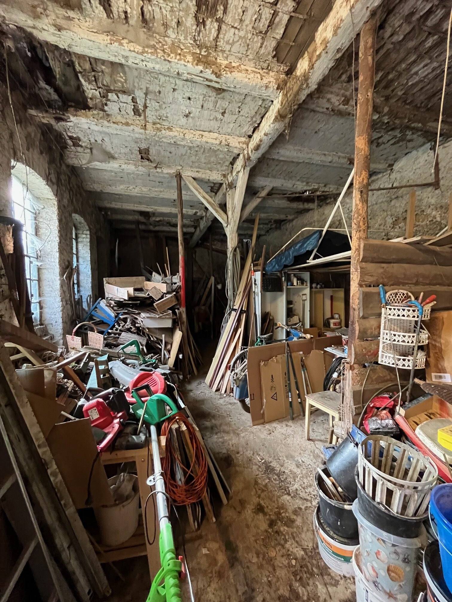 Lagerraum mit Gartengeräten, Eimern, Kartons und Holz bis unter die Decke