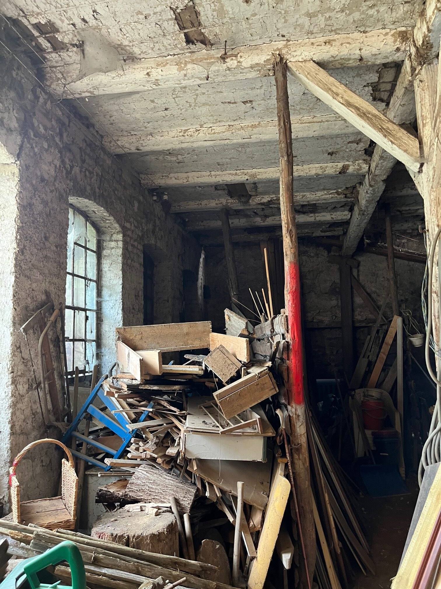 Vollgestellter Innenraum mit Kisten, Fahrrädern und Holz unter einem alten Deckenbalken